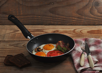bacon and eggs and mushrooms with the pan on wooden background i