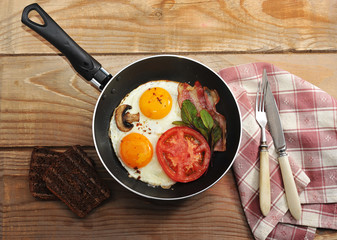 bacon and eggs and mushrooms with the pan on wooden background i