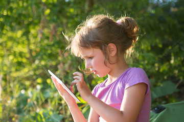 kid hold tablet, phone for playing and education. Little girl using a tablet outdoors.

