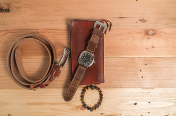 Men's accessories with brown leather wallet, bracelet, belt and watch on wood background
