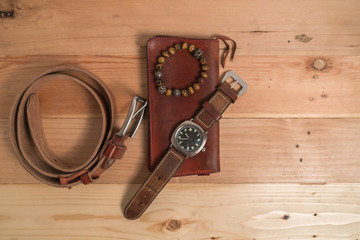 Men's accessories with brown leather wallet, bracelet, belt and watch on wood background
