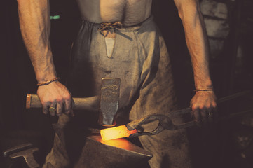Blacksmith working metal with hammer on the anvil