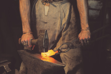 Blacksmith working metal with hammer on the anvil