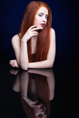 Young woman with ginger hair over reflection mirror on blue back