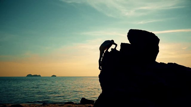 Man climbs on a rock at sunset on the beach-1