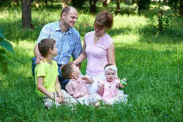 Naklejka na ściany i meble happy family portrait on outdoor, group of five people sit on grass in city park, summer season, child and parent