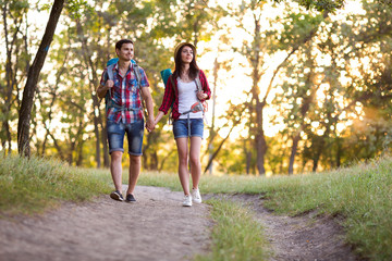 Young Couple Man and Girl in casual Travel Clothing with Backpacks walking on Forest Trail talking and enjoying sightseeing