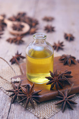 Essential aroma anise oil in a glass bottle with dried star anise on wooden spoon and background.