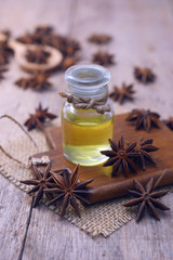 Essential aroma anise oil in a glass bottle with dried star anise on wooden spoon and background.