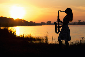 silhouette portrait of a woman in a dress whose hobby music, she plays on the river bank and is...