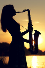 portrait of a woman in a dress playing the saxophone near the river