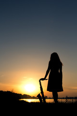 silhouette of a woman in a dress on a background of a beautiful sun set and the sky saxophone on...