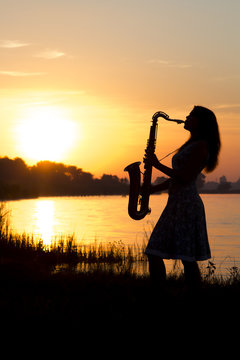 silhouette of a young woman playing a wind instrument at dawn on the river