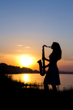 silhouette of a young woman playing a wind instrument at dawn on the river