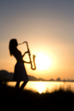 blurred silhouette portrait of a woman in a dress whose hobby music, she plays on the river bank and is resting emotionally