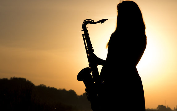 female silhouette against the dawn with a saxophone in his hands