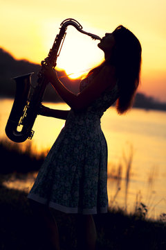 portrait of a woman in a dress playing the saxophone near the river