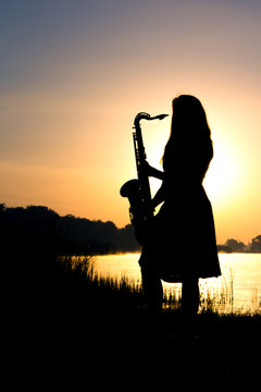 silhouette of a girl in a dress with a brass musical instrument in his hands looking thoughtfully into the distance