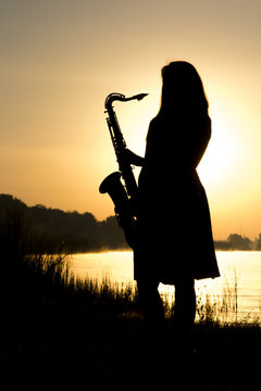 female silhouette against the dawn with a saxophone in his hands