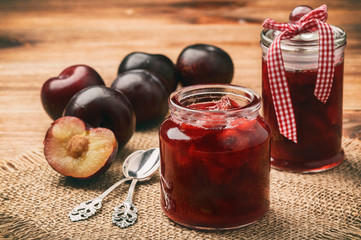 Plum jam in glass jars on wooden background.