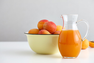 Glass jug with fresh juice and ripe apricots bowl