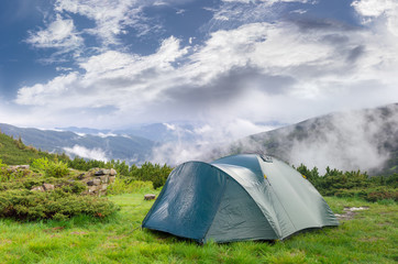 Hiking tent after rain on background of mountains and sky