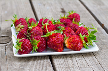 Ripe red strawberries on white plate on a wooden background