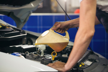 Auto mechanic is changing motor oil into a engine at car station