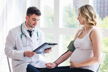 Fototapeta premium Young doctor checking blood pressure of a pregnant woman
