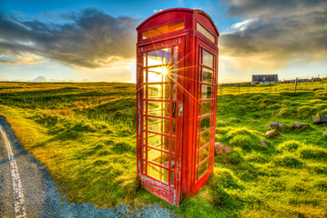Urban red telephone box in the middle of a green countryside. Concept for synergy between modern and rural area. Red and green complementary colors join together in a scottish land, United Kingdom.