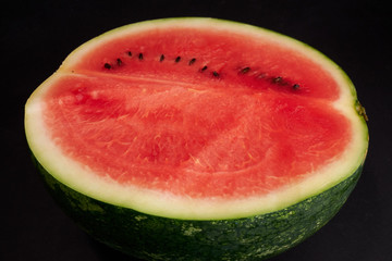Water melon cut in half with pink flesh and green rind on the black background