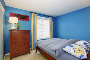 Blue interior of a small bedroom with brown dresser