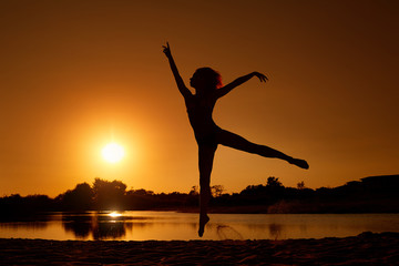 Silhouette of a woman jumping at the beach in the sun at sunset.