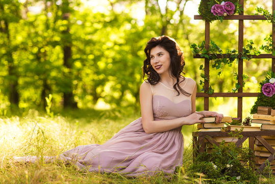 woman in elegance dress sits on the ground in the wood near decorations