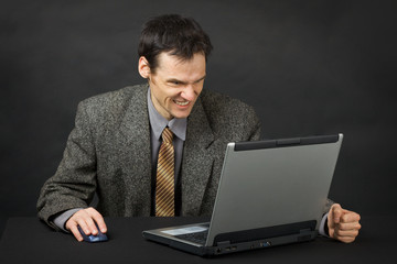 Furious man sits at table and looks at laptop screen