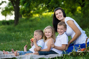 Happy mother, two sons and daughter dressed in white shirts are sitting on the grass in the park