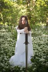 Beautiful woman wearing a long white dress holding a medieval sword