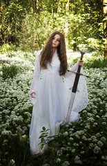 Beautiful woman wearing a long white dress holding a medieval sword