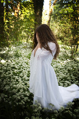 Woman wearing a  long white dress standing in a forest