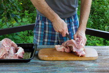 a white man cuts fresh pork meat on the background of nature. selective focus