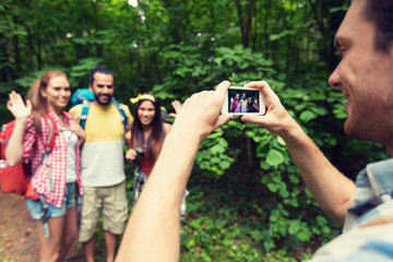 happy man photographing friends by smartphone