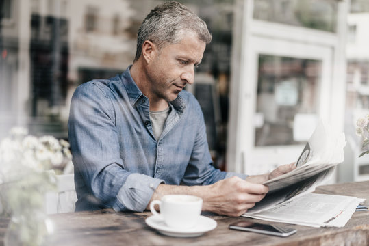 Mature man sitting in cafe reading newspaper