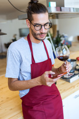 Handsome young man using his mobile phone in the kitchen.