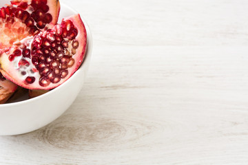 Pomegranate in bowl on white wooden background

