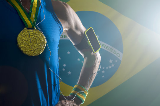 Brazilian gold medal athlete standing with mobile phone armband and headphones against dramatically lit Brazil flag background