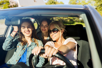 happy teenage girls or young women driving in car