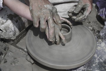 A men's hands guiding a child hands to help him to work with raw clay