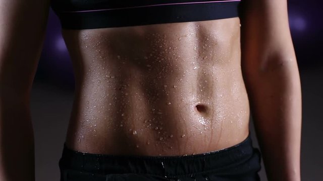 Water drops pouring down ideal flat tummy of sportive woman training in gym