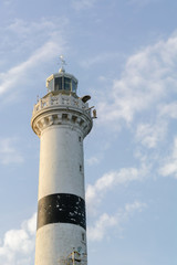 high white stone lighthouse with a black stripe on a blue evening sky with clouds