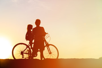 Fototapeta na wymiar Silhouette of father and little daughter biking at sunset